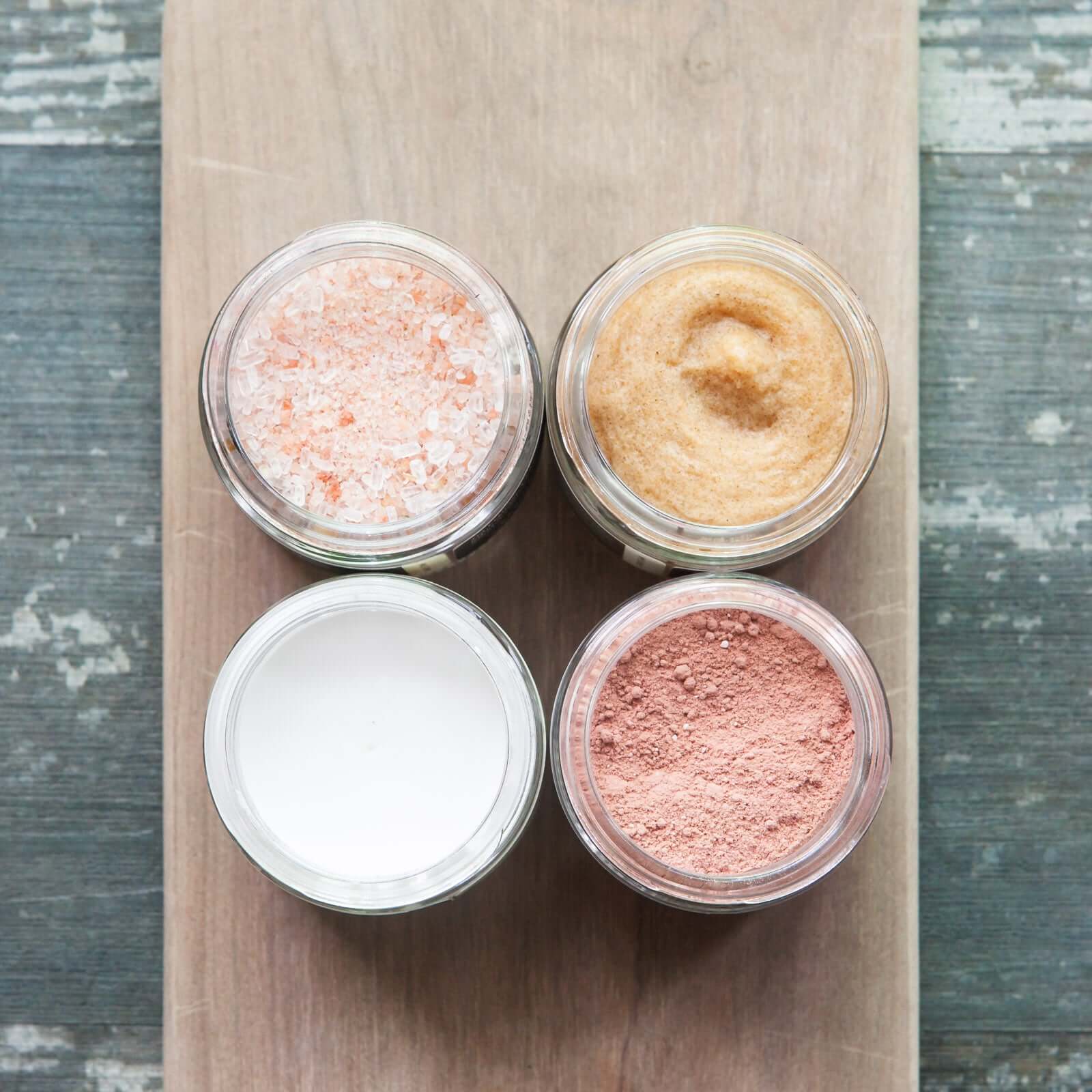 Body butter, body scrub, bath soak, and dry mask in jars on a wooden board