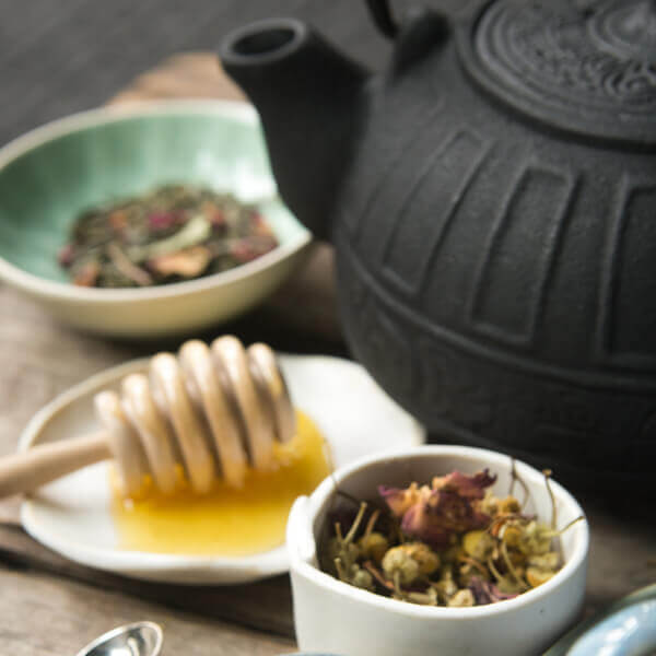 Bowls of loose-leaf tea and a plate of honey next to a tea kettle 