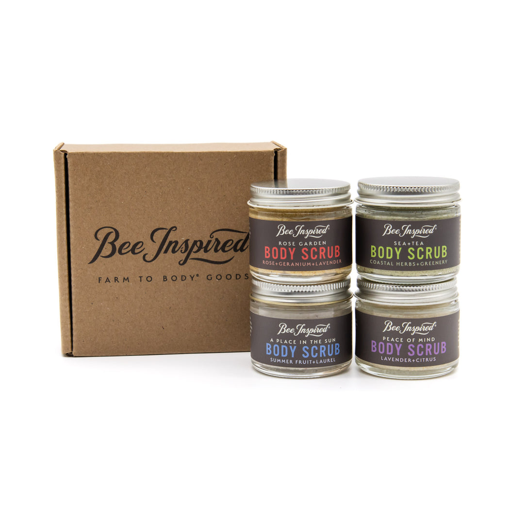 Four jars of Bee Inspired body scrub with a cardboard box on a white background