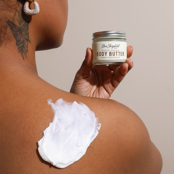 Person applying body butter to their shoulder with a container labeled &
