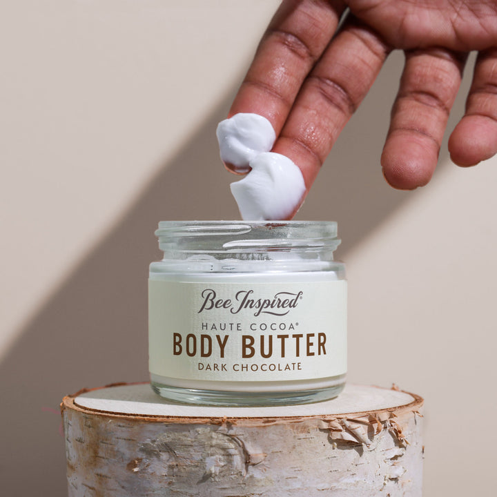 Hand applying body butter to a jar labeled &