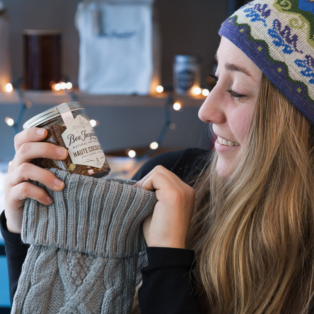 Person wearing a knitted hat and scarf holding a jar of haute cocoa chai