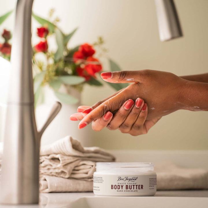 woman using haute cocoa body butter from bee inspired honey retail store in owings mills on her hands next to a sink 