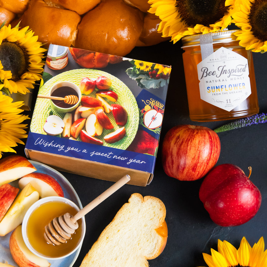Gift box with apples, honey, and sunflowers on a dark surface