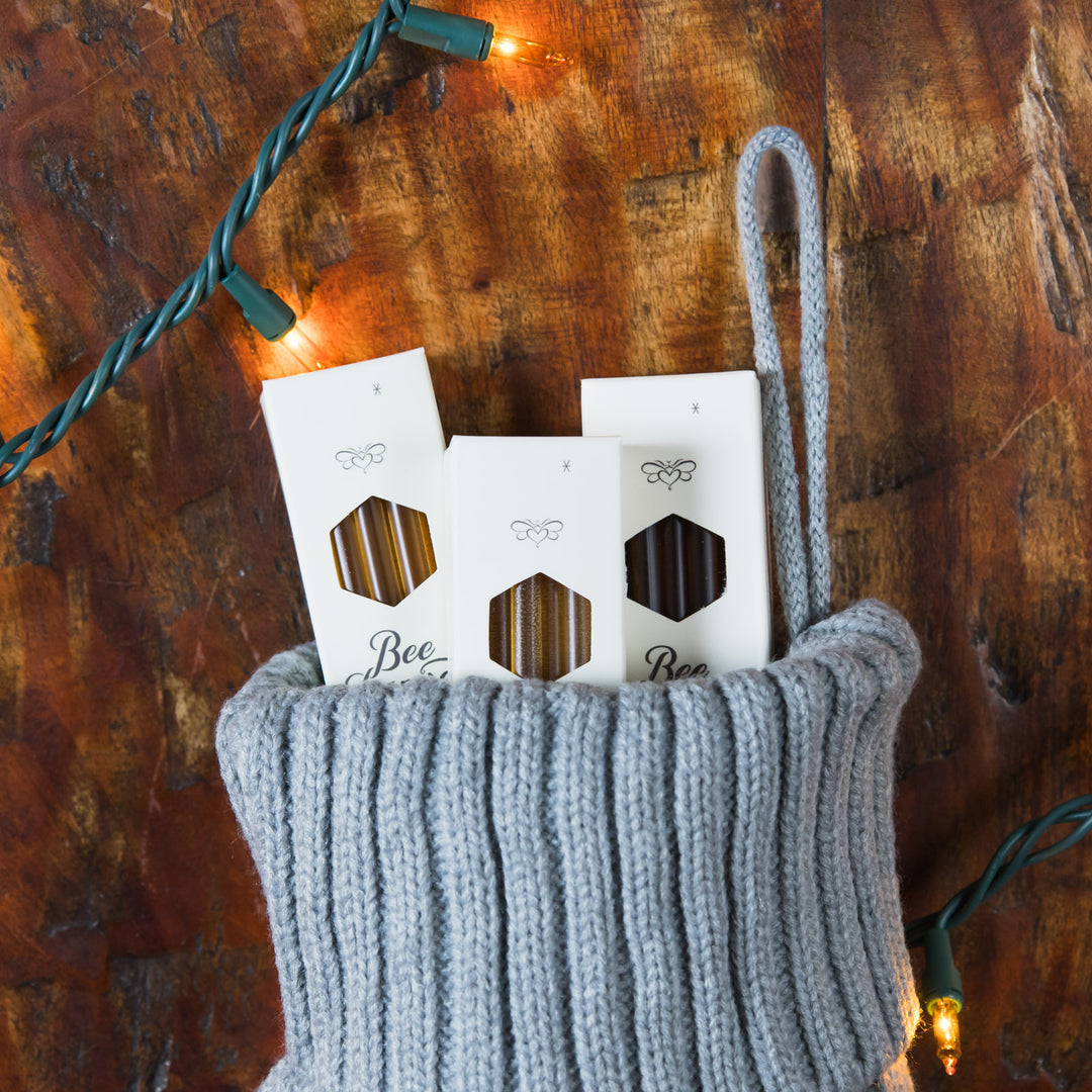 Gray knitted stocking with honey sticks inside on a wooden surface with string lights.
