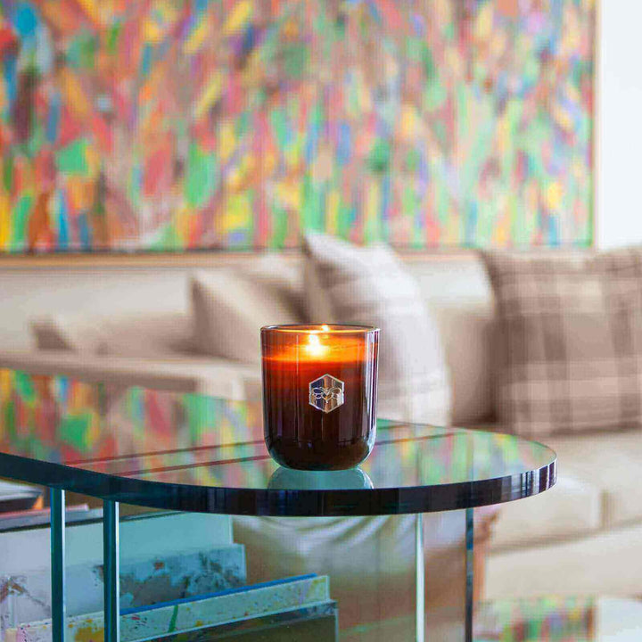 Luxe candle burning on glass table in front of colorful wall 