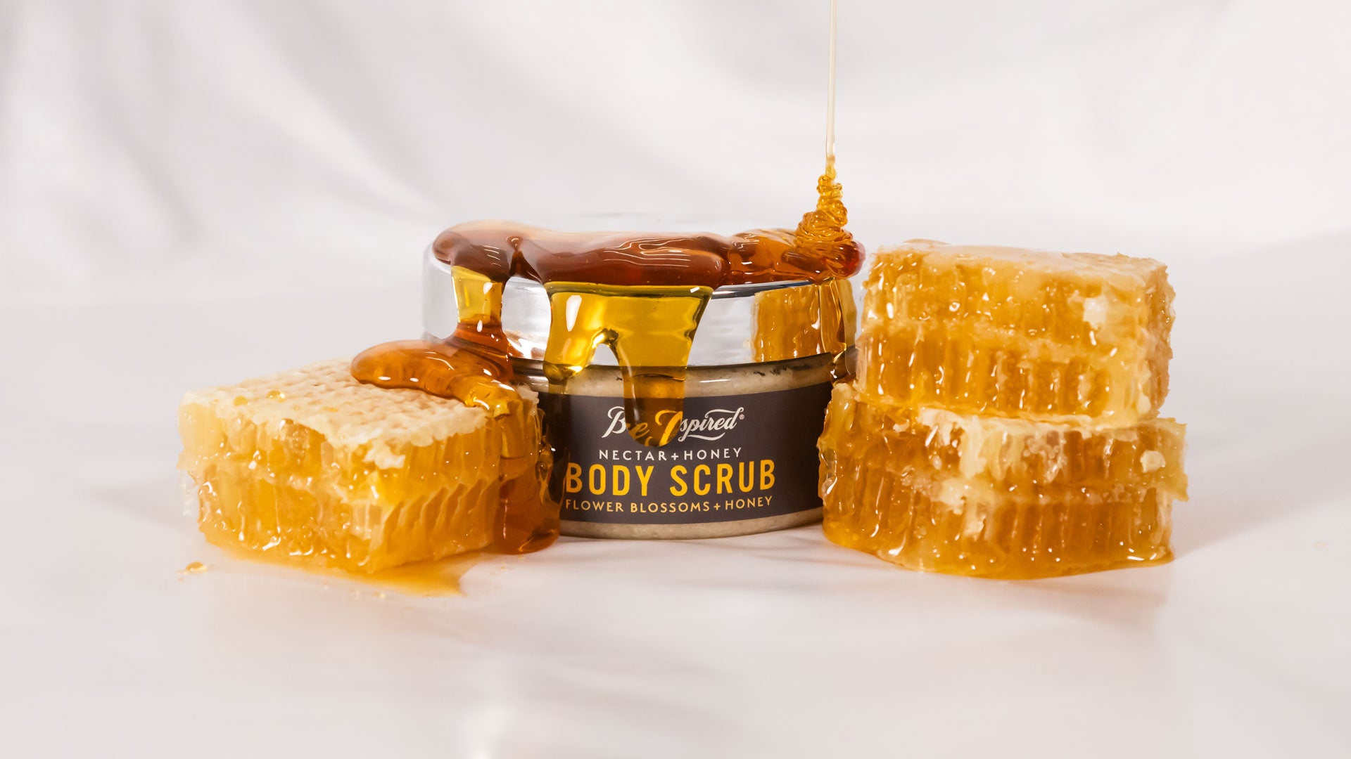 nectar + honey body scrub next to honeycomb being drizzled with honey
