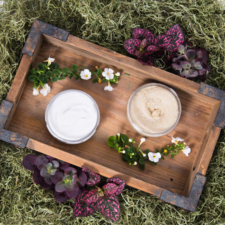 Two bowls of cream on a wooden tray with decorative plants on a grassy background