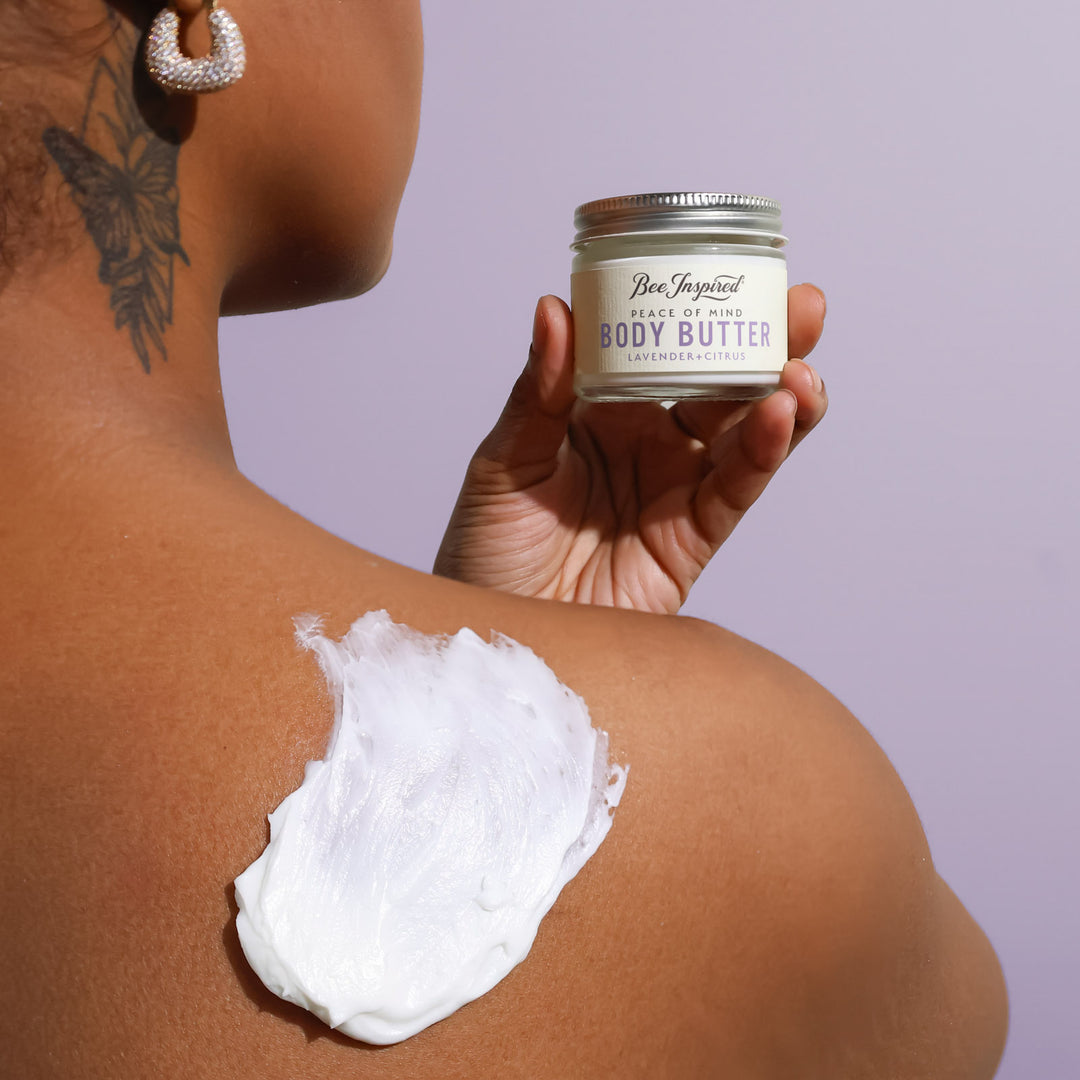 Person applying body butter to their shoulder with a jar labeled &