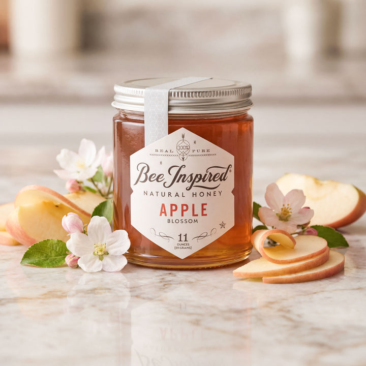 Jar of Bee Inspired natural honey with apple blossoms and slices on a marble surface