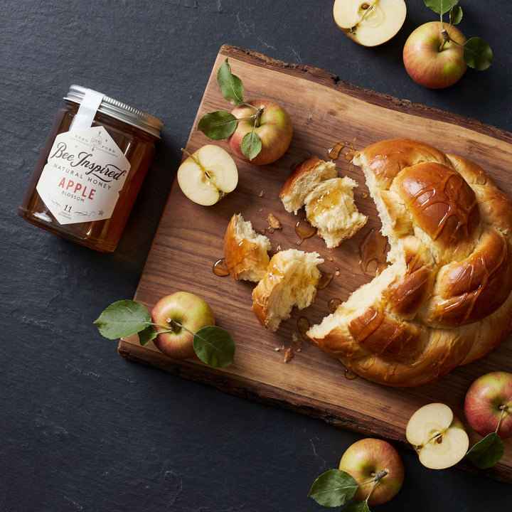 Braided bread with apples and a jar of apple honey on a wooden board.