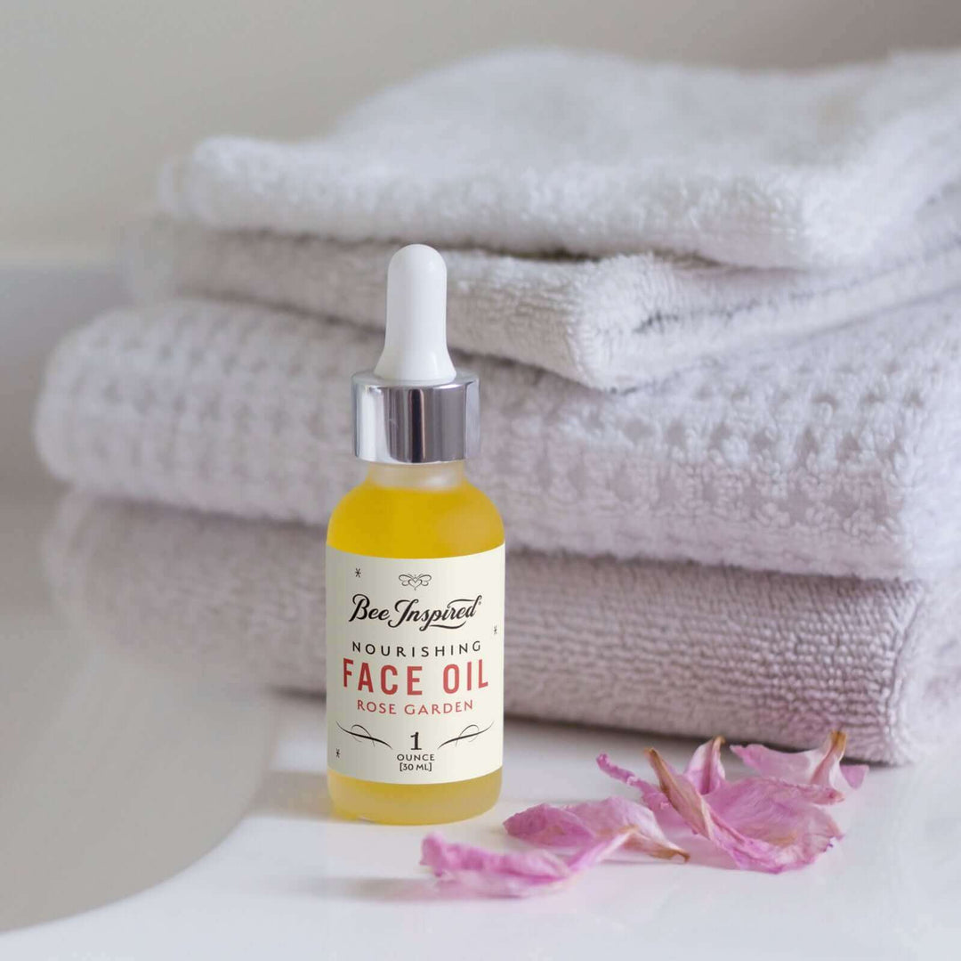 Bee Inspired rose face oil next to a flower petals and a stack of towels 