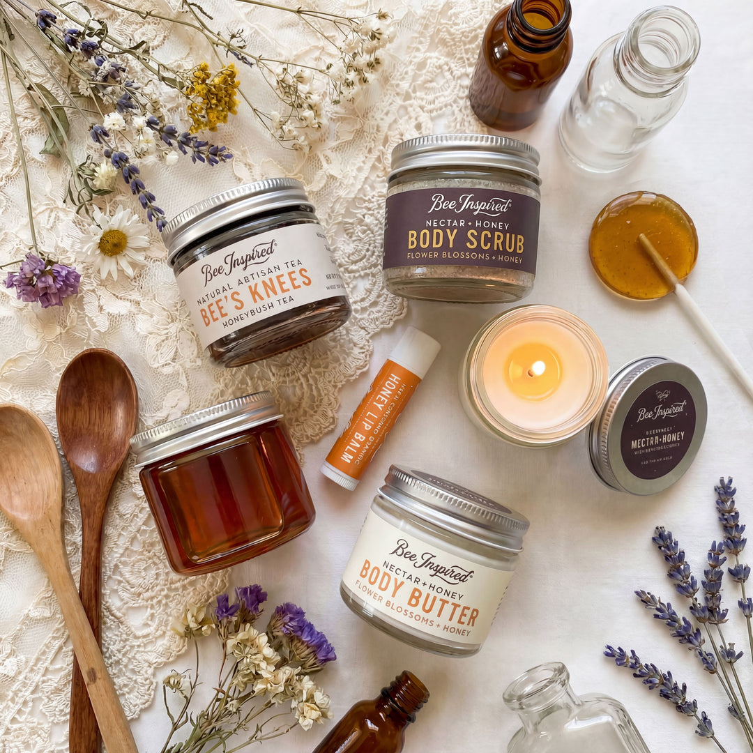 Collection of Bee Inspired products including jars, bottles, and a candle on a textured surface with flowers.