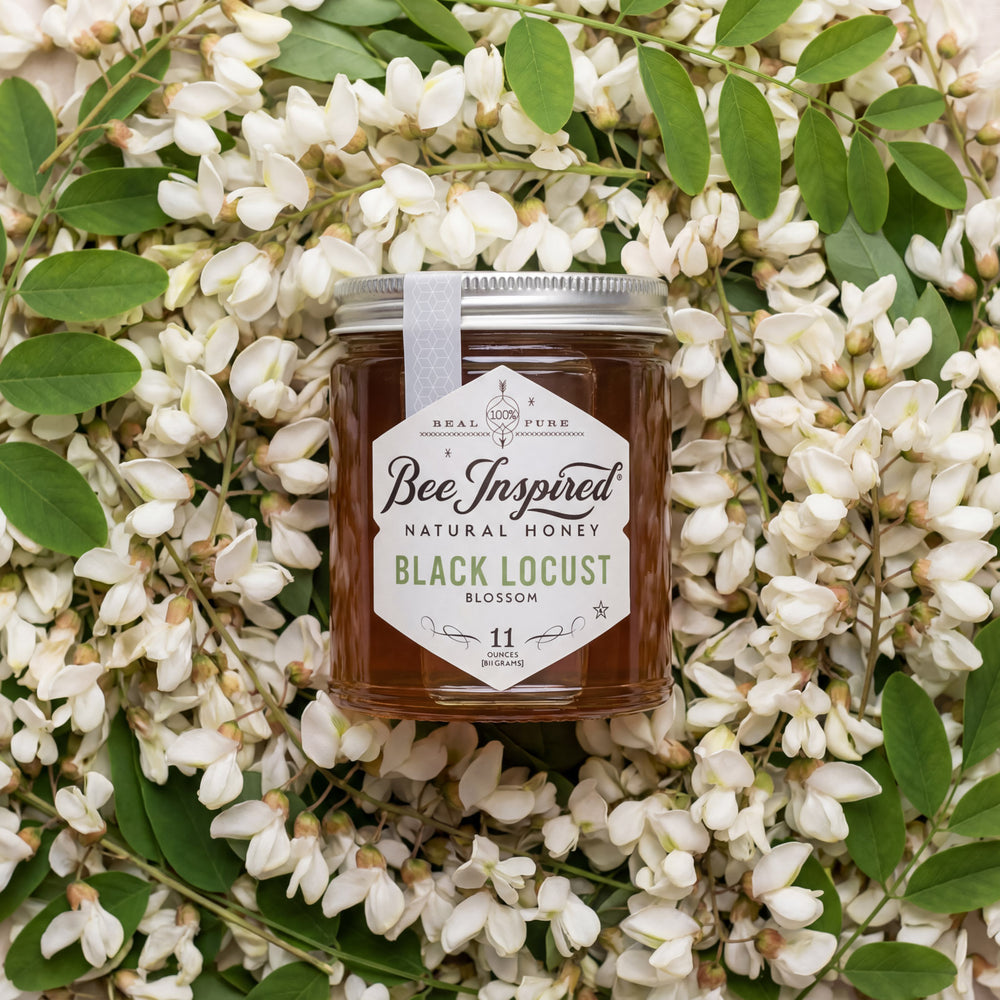 Jar of Bee Inspired honey surrounded by white flowers and green leaves