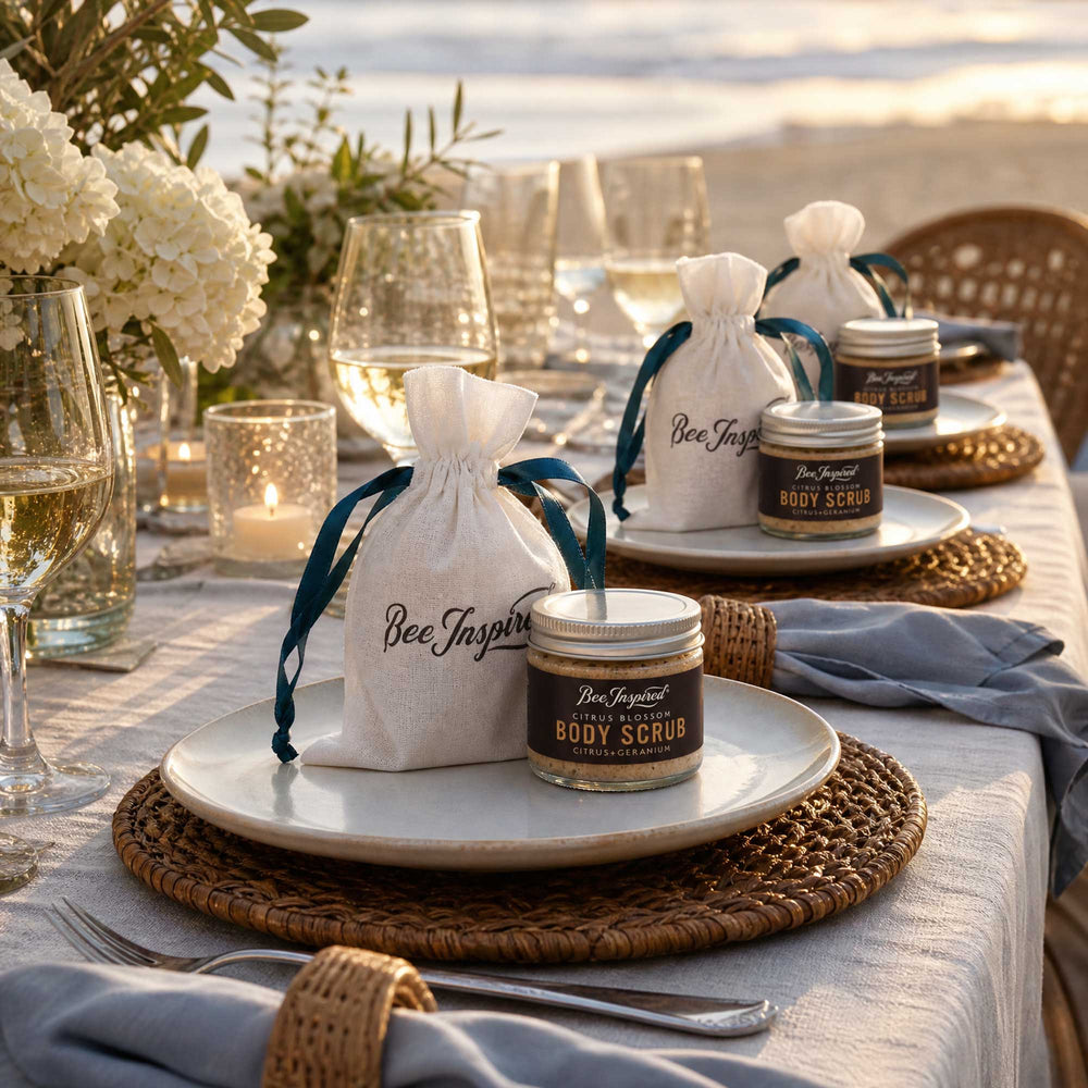 Table setting with 'Bee Inspired' body scrub party favors and bags on a sunset background.