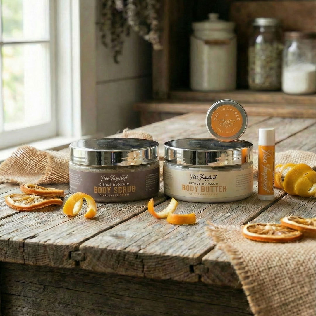 Body care products including body scrub, body butter, and a bottle on a rustic wooden table with dried oranges.