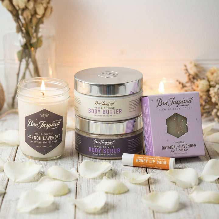 Bee Inspired product line including a candle, body butter, scrub, soap, and lip balm on a wooden surface with flowers.