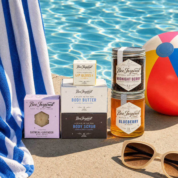 Bee-Inspired products including a jar, bottle, and boxes by a poolside with a towel and beach ball.