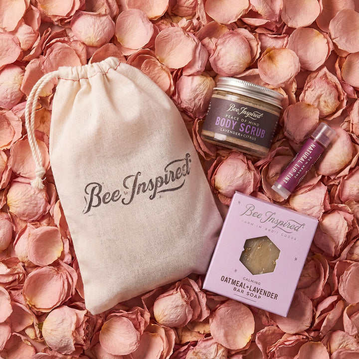 Bee Inspired beauty products including a jar, bar soap, and pouch on pink flower petals.