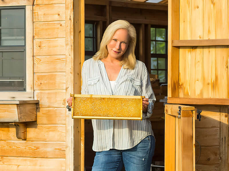 Kara holding a hive frame in doorway of cabin 