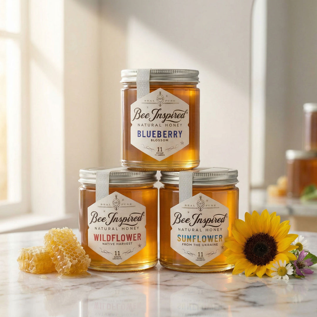 Three jars of 'Bee Inspired' honey stacked on a marble surface with flowers and honeycomb.