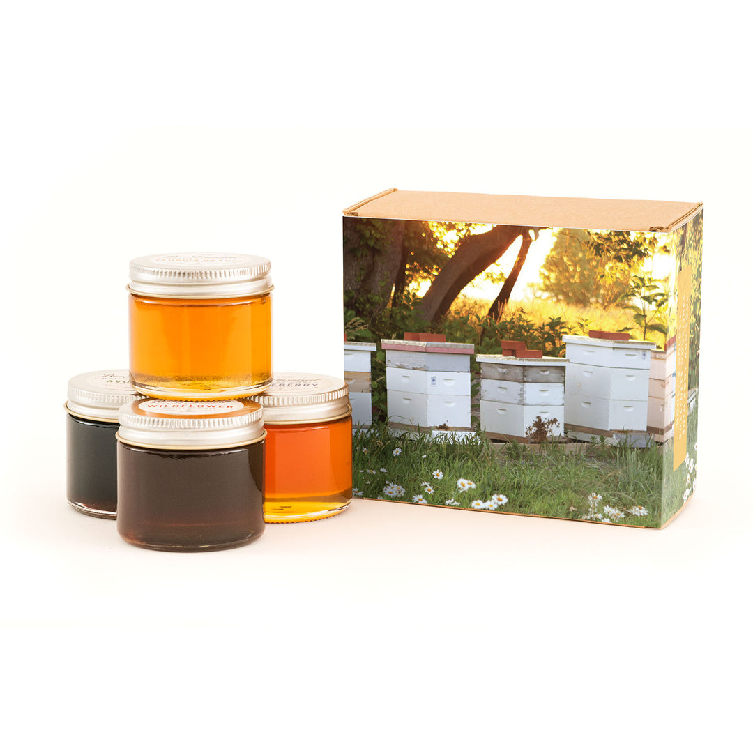 Jars of honey with a box featuring beekeeping imagery on a white background
