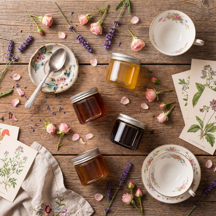 Jars of honey, tea cups, and floral elements on a wooden surface