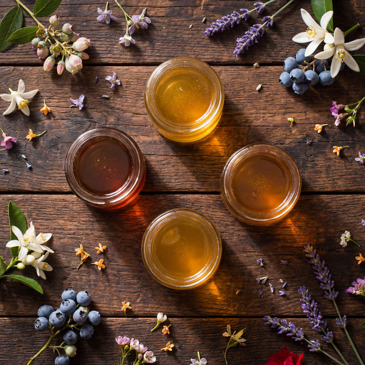 Four jars of honey on a wooden surface with flowers and berries.