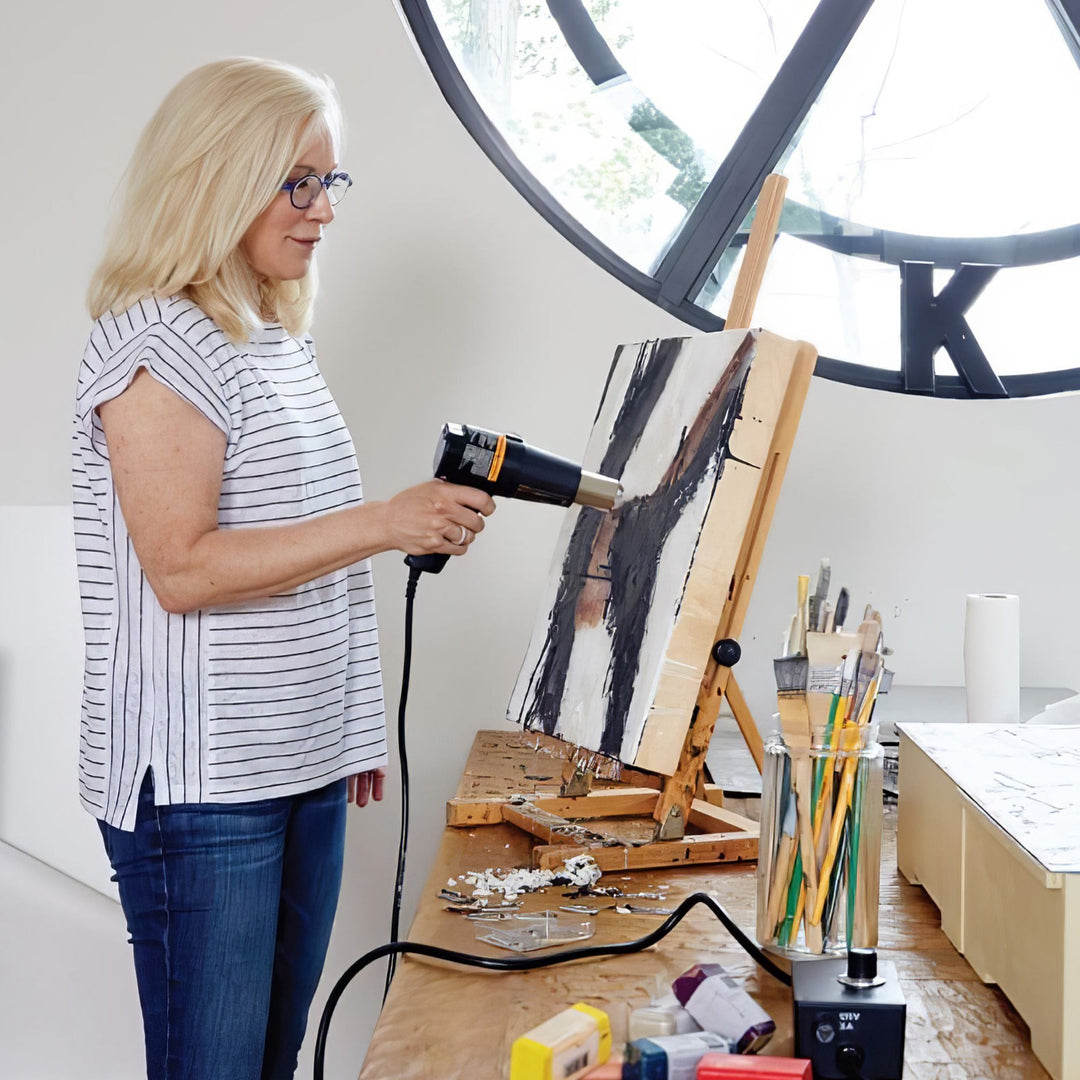 Kara using a hair dryer on an encaustic painting in a studio setting