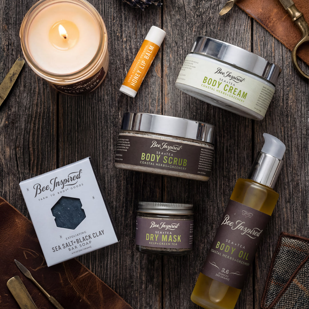 Collection of Bee Inspired skincare products on a wooden surface with a lit candle.