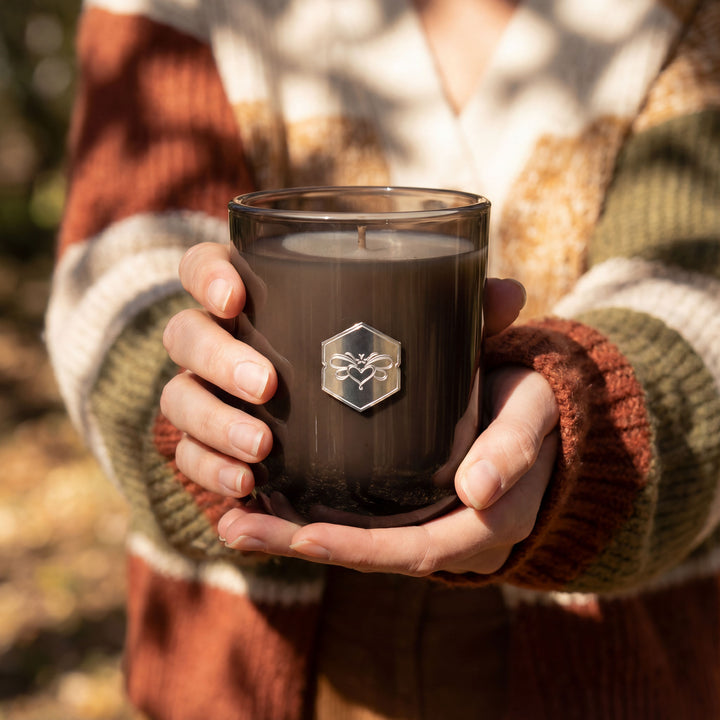 Person holding a dark glass candle with a logo, wearing a patterned sweater.