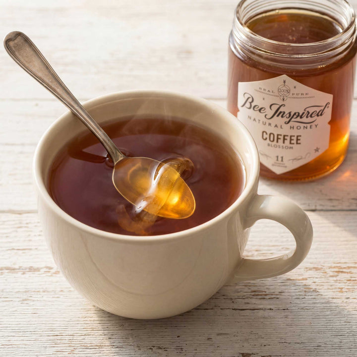 Honey being drizzled into a cup of coffee with a jar of honey labeled &