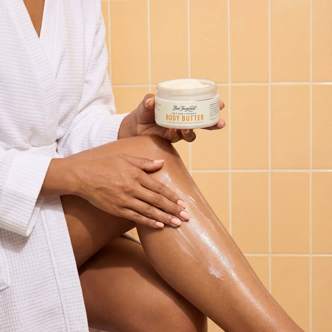 Person applying body butter to their leg in a bathroom setting