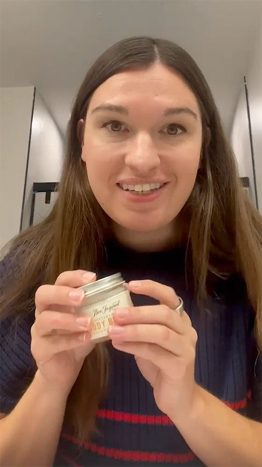 Person holding a small container with a label, standing in a bathroom.