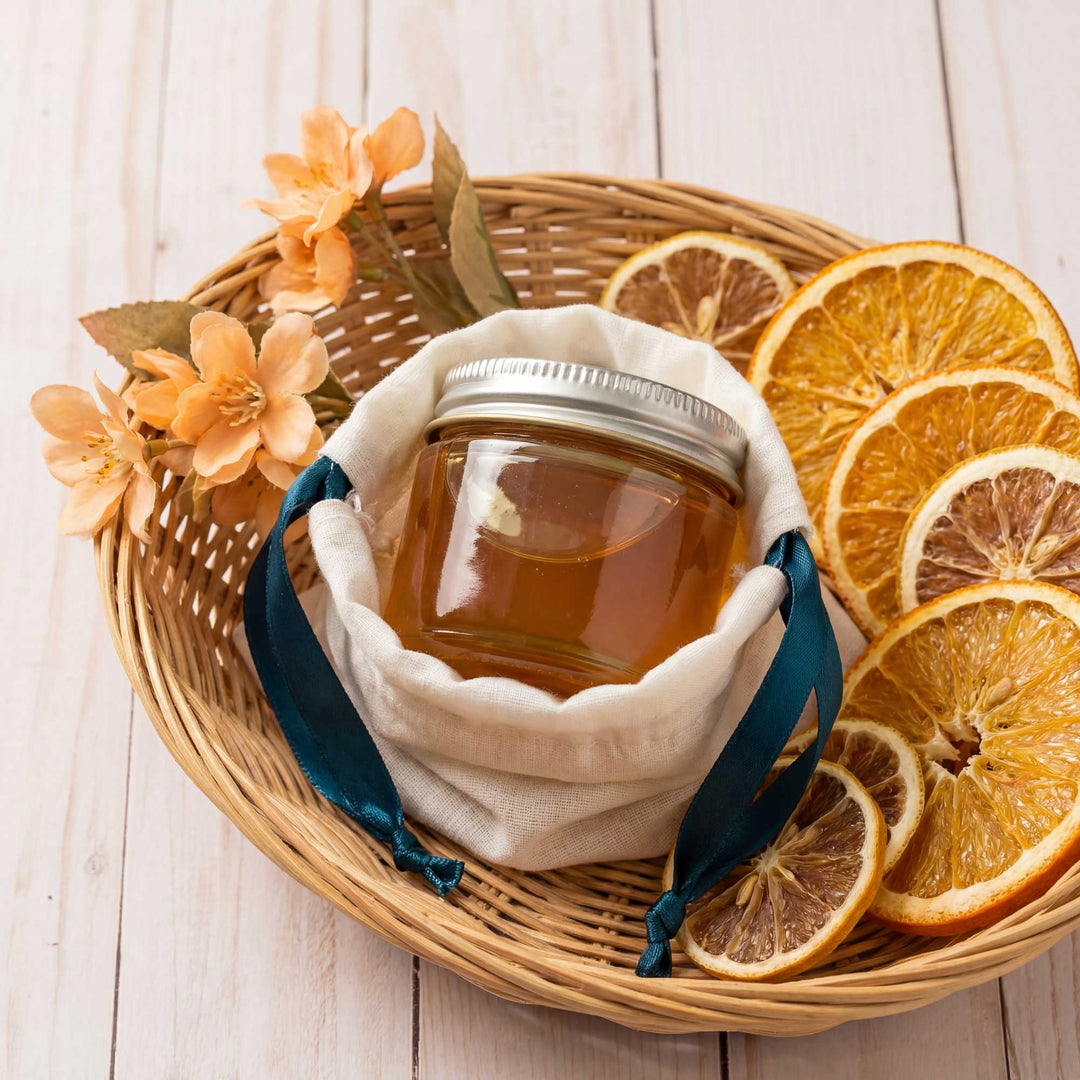 Jar of honey in a cloth bag with dried oranges and flowers on a wooden surface