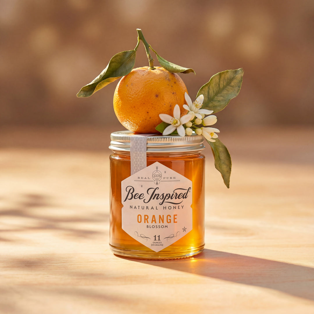 Jar of 'Bee Inspired' Orange Blossom honey with an orange and flowers on a wooden surface.