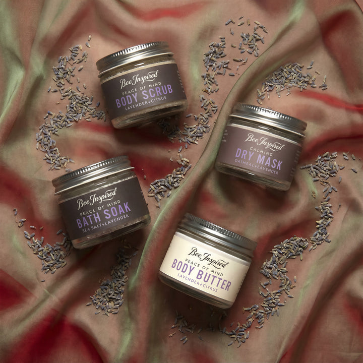 Four containers of Bee Inspired body care products on a textured fabric background with lavender.