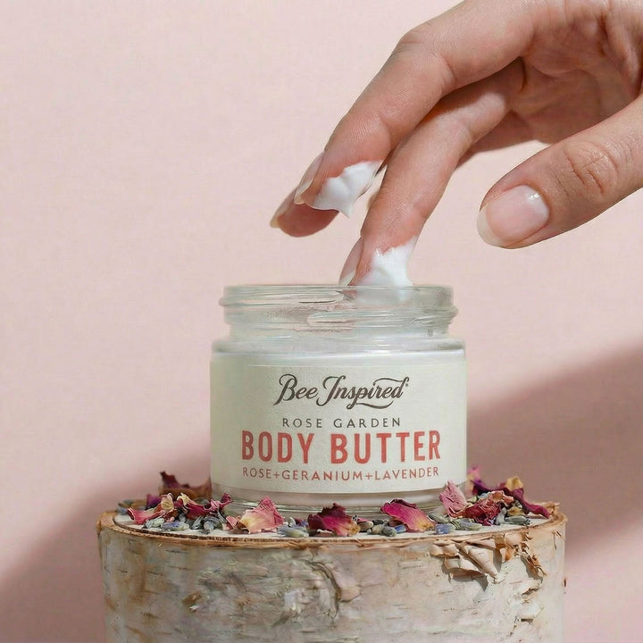 Hand applying body butter from a jar labeled &