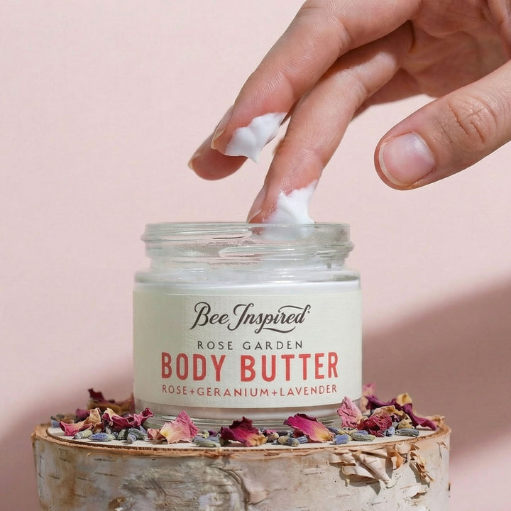 Hand applying body butter from a jar labeled &
