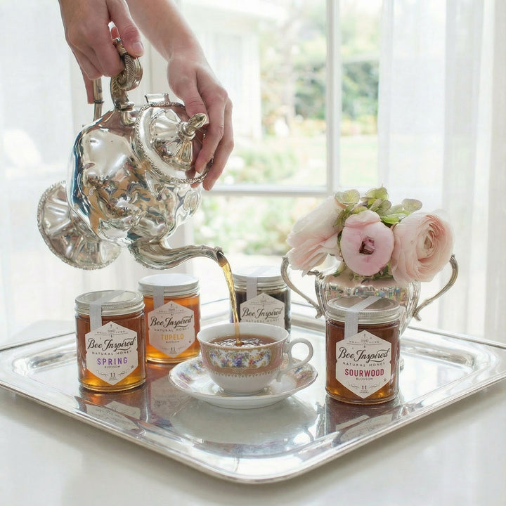 Tea being poured from a silver teapot into a cup on a tray with jars and flowers.