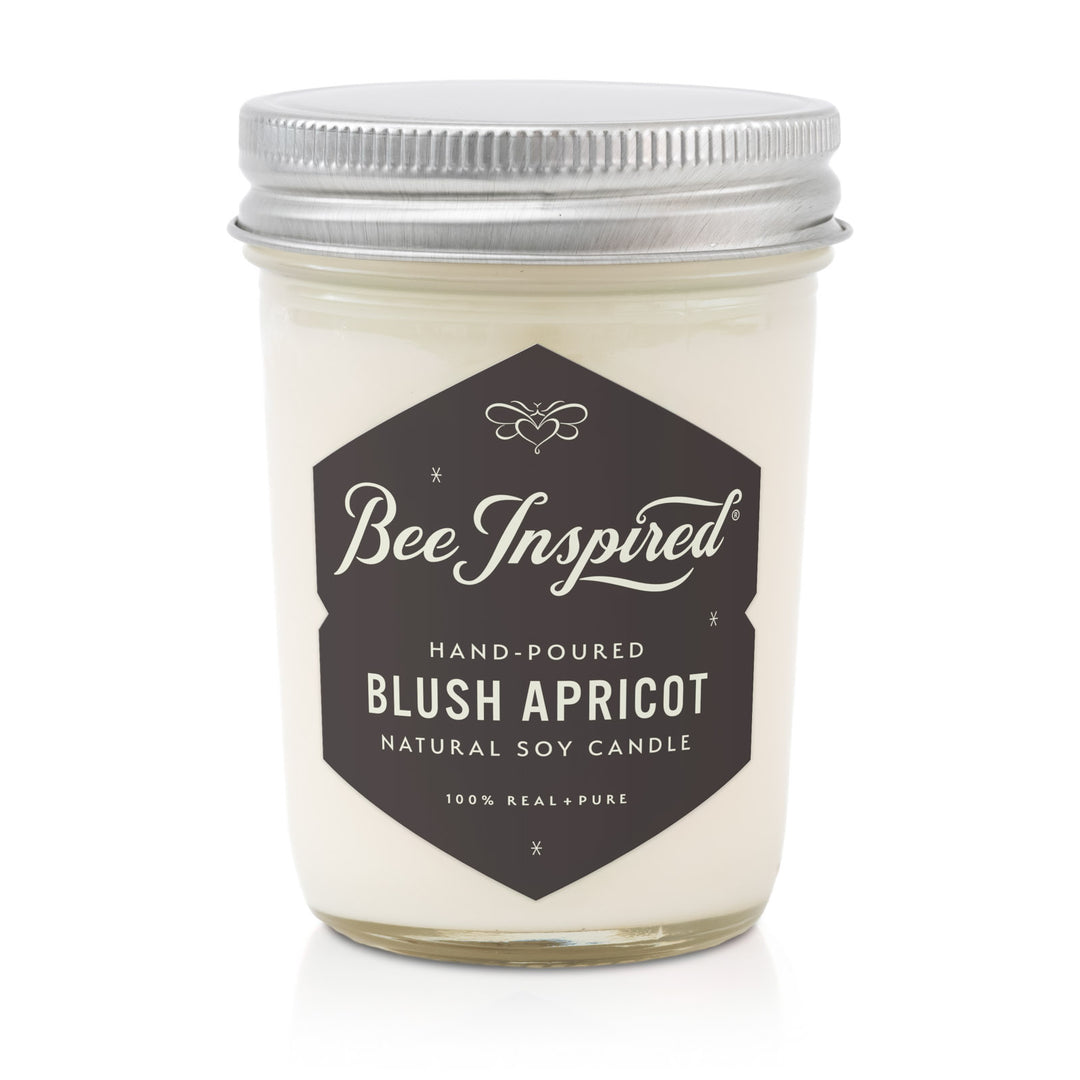 Candle jar labeled 'Bee Inspired' with 'Blush Apricot' scent on a white background