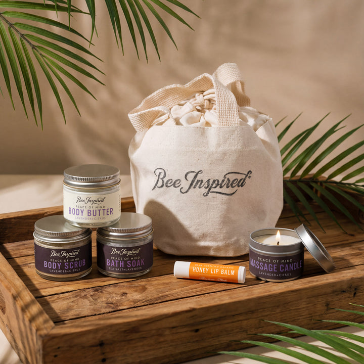 Collection of Bee Inspired beauty products including candles, lip balm, and body scrub on a wooden tray with a &