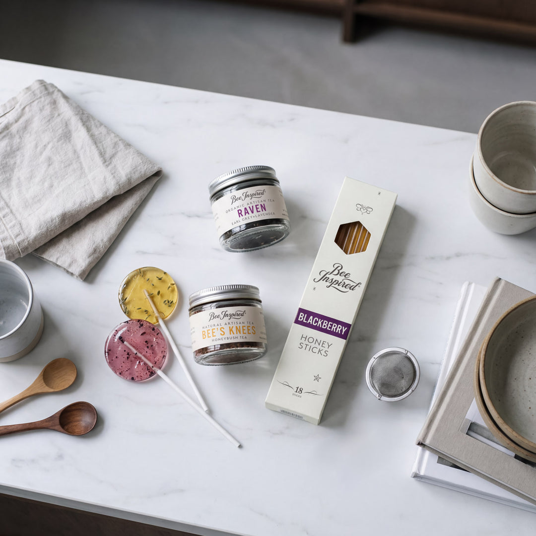 Tabletop scene with Bee &amp; Raven products including jars, a box, and honey sticks on a marble surface.