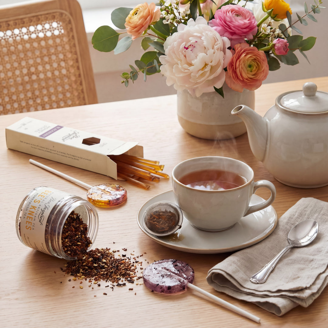 Tea-making setup with a cup of tea, teapot, and floral arrangement on a table.