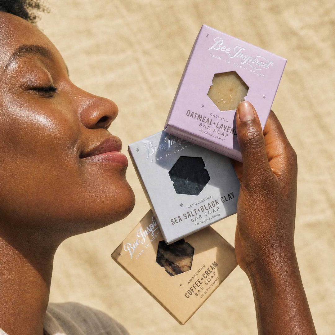 Woman holding three different soap bars with visible branding against a neutral background