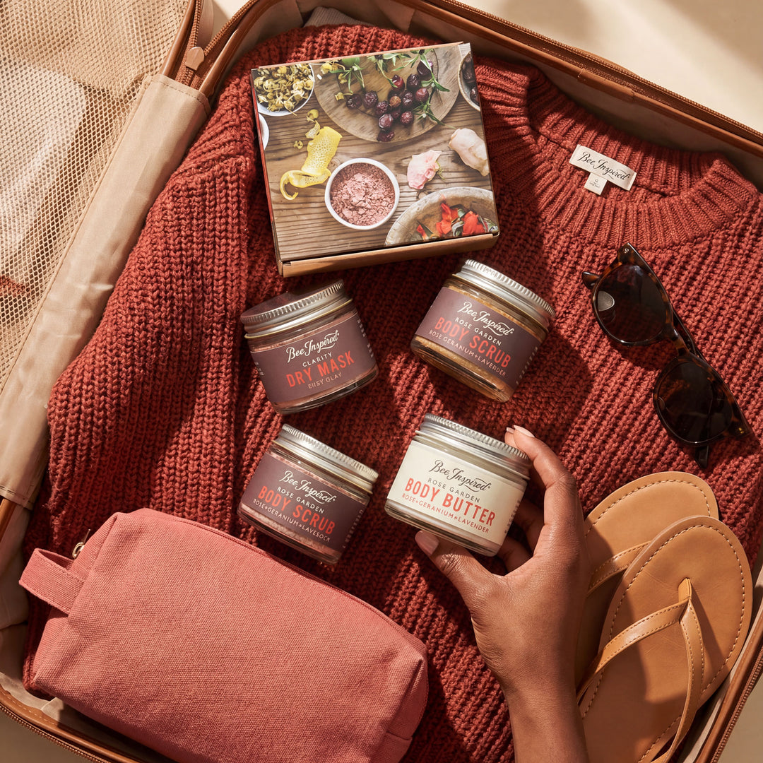 Collection of body care products on a textured surface with a hand holding a jar.