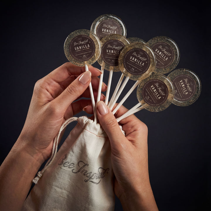 Hands holding vanilla extract pods above a drawstring bag with &