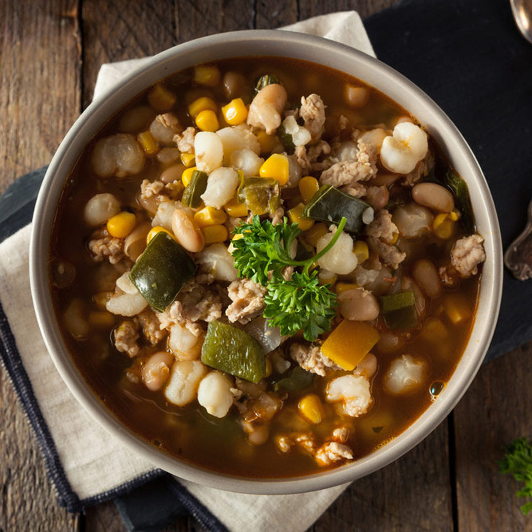  bowl of hearty soup with beans, corn, and ground meat on a wooden table